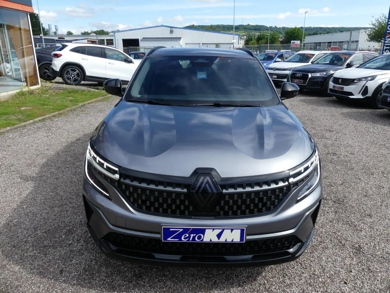 Vue avant d'un Renault Austral gris métallisé avec calandre à damier et logo Alpine noir, en extérieur sur parking.