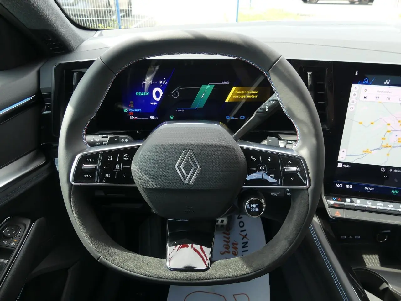 Vue rapprochée du volant Alcantara noir avec surpiqûres bleues du Renault Austral 2025, tableau de bord digital et écran tactile.