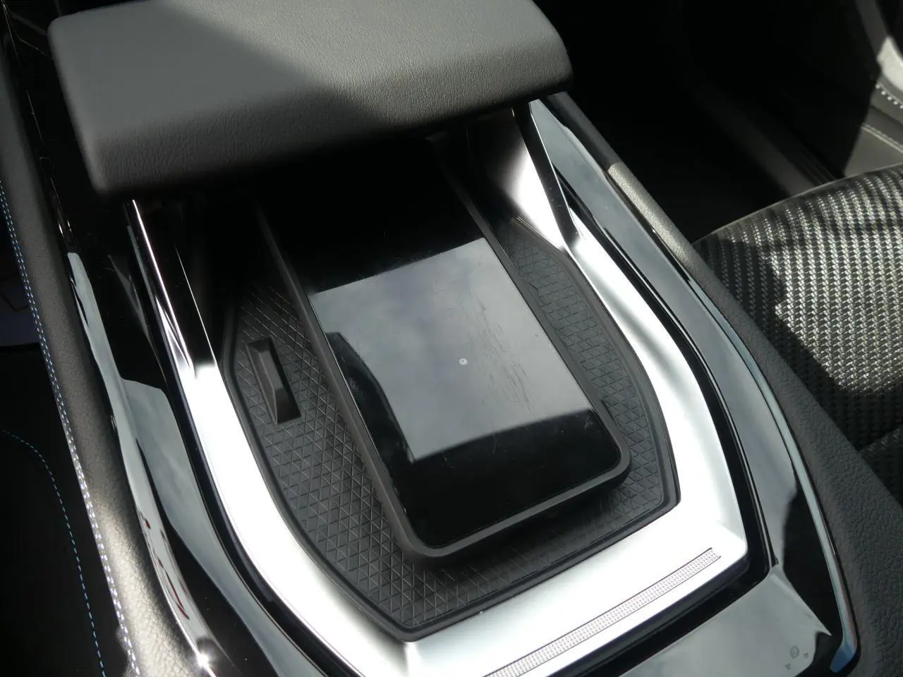 Gros plan sur la console centrale noire brillante du Renault Austral 2025 avec chargeur smartphone par induction et sellerie tissu Alcantara.