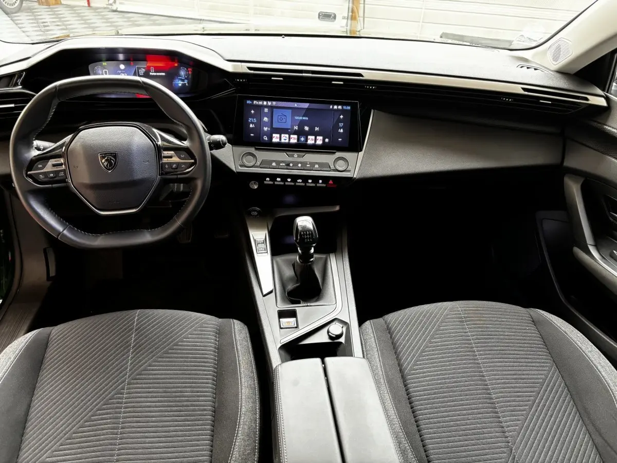 Intérieur de la Peugeot 308 2022 vue de face, volant cuir, écran tactile central et levier de vitesse manuel visibles.