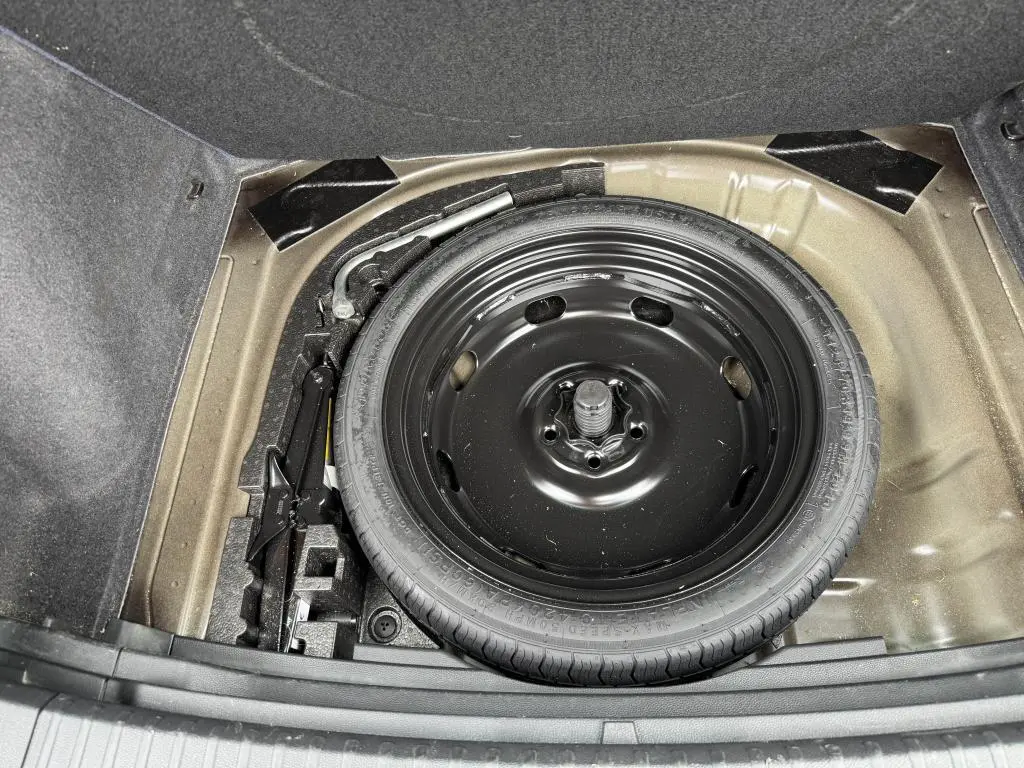 Roue de secours noire et outils de bord dans le coffre du SEAT Ateca 2023, vue plongeante sur l'espace de rangement.