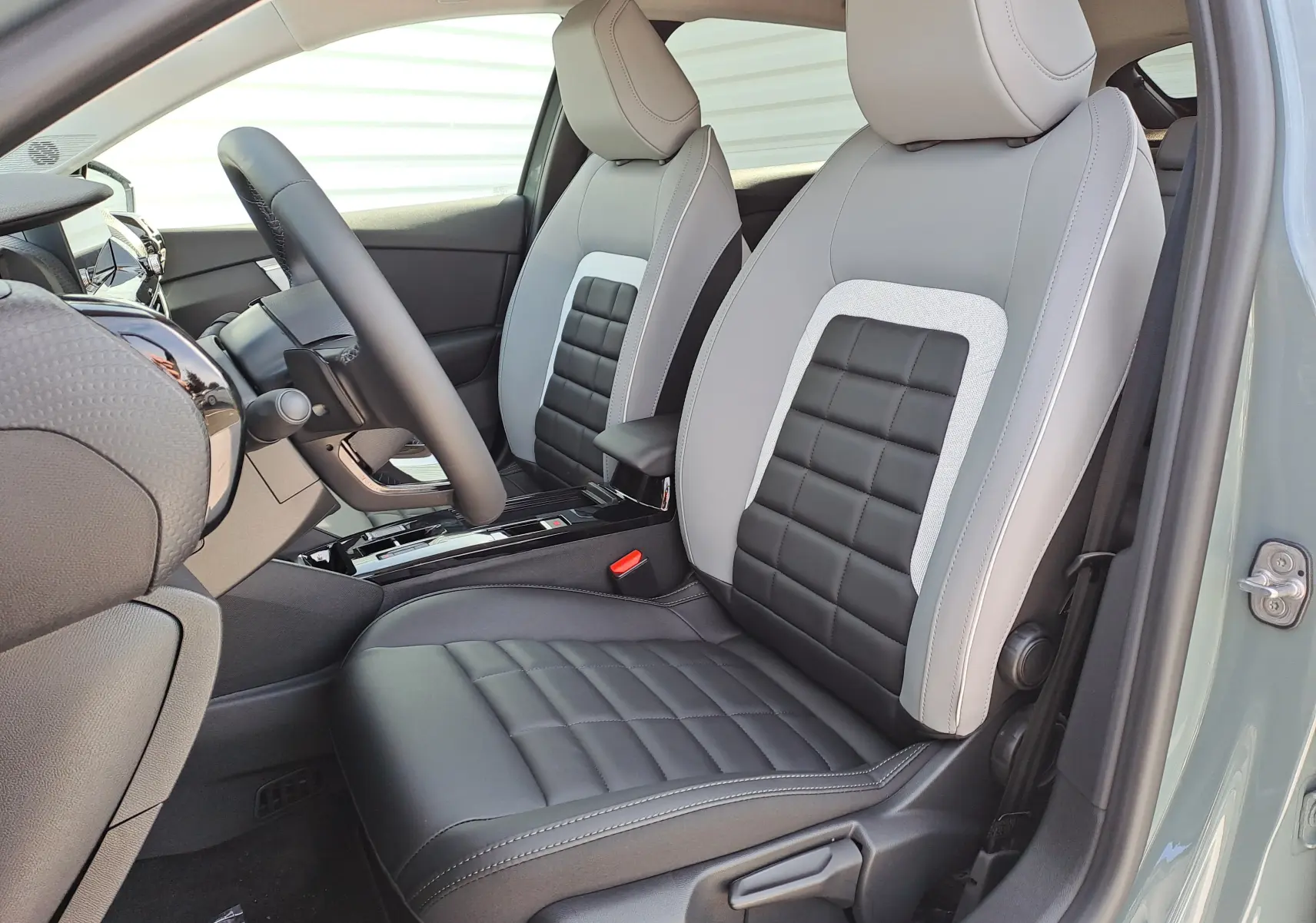 Vue intérieure côté conducteur de la Citroën C4 hybride 2025 avec sièges bicolores gris clair et noir, volant et console centrale visibles.