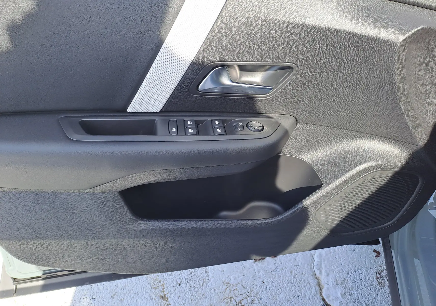 Détail de la porte côté gauche de la Citroën C4 hybride 2025 Manhattan Green, avec commandes de vitres et poignée argentée.