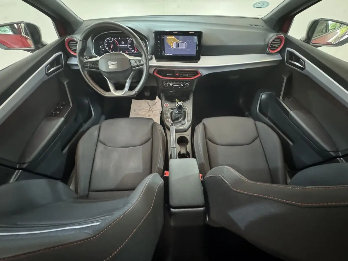 Vue intérieure avant du tableau de bord et des sièges noirs de la SEAT IBIZA 1.0 TSI 110 FR avec volant cuir et écran tactile central.