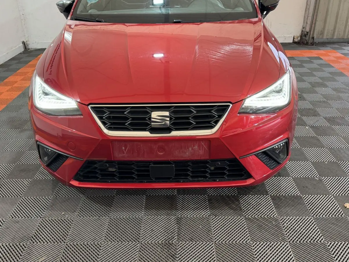 Vue frontale d'une SEAT IBIZA 1.0 TSI 110 FR rouge avec phares LED allumés et calandre hexagonale noire.