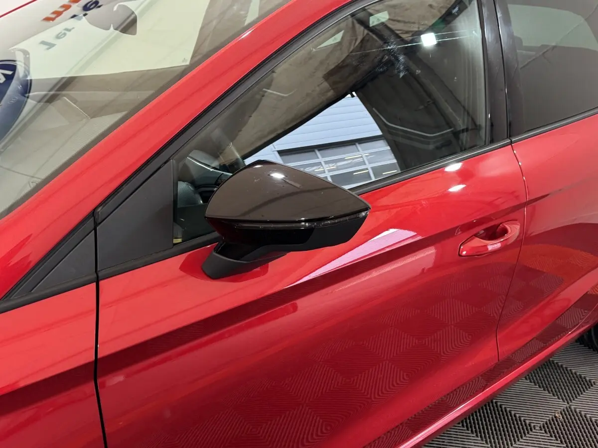 Détail du côté gauche rouge vif de la SEAT IBIZA 1.0 TSI 110 FR avec rétroviseur noir brillant et poignée de porte intégrée.