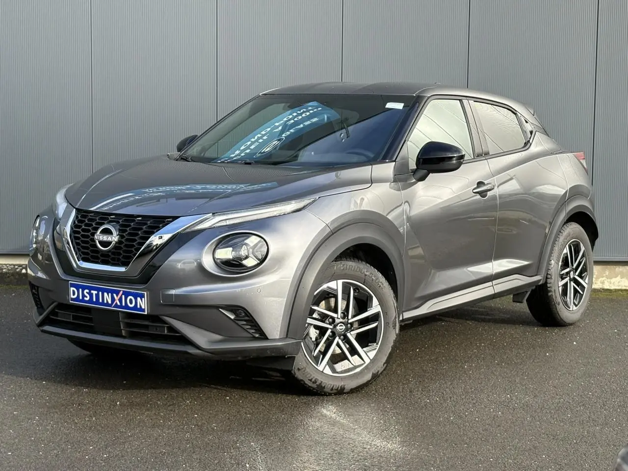 Nissan Juke gris foncé en 3/4 avant droit, avec jantes alliage 17'' et calandre noire distinctive.