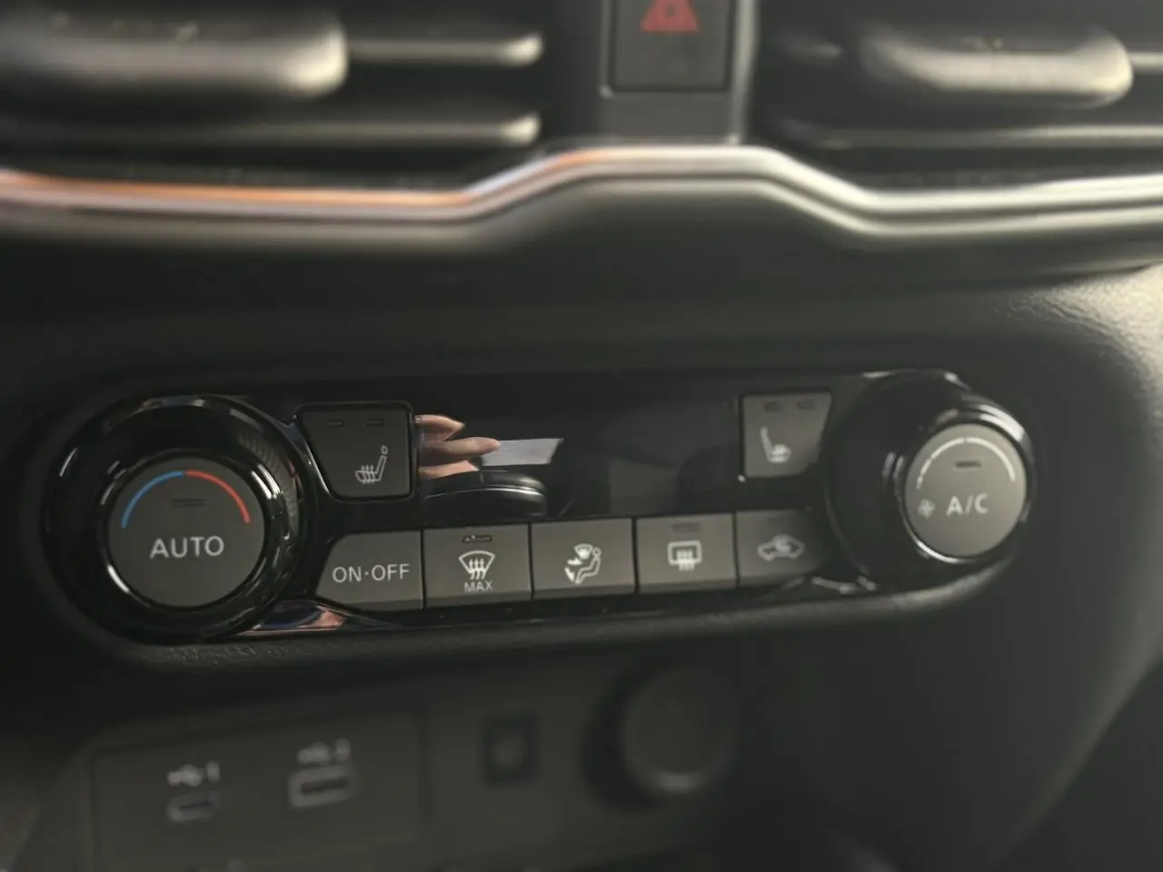 Gros plan sur la console centrale noire du Nissan Juke 2025 montrant les commandes de climatisation automatique et sièges chauffants.