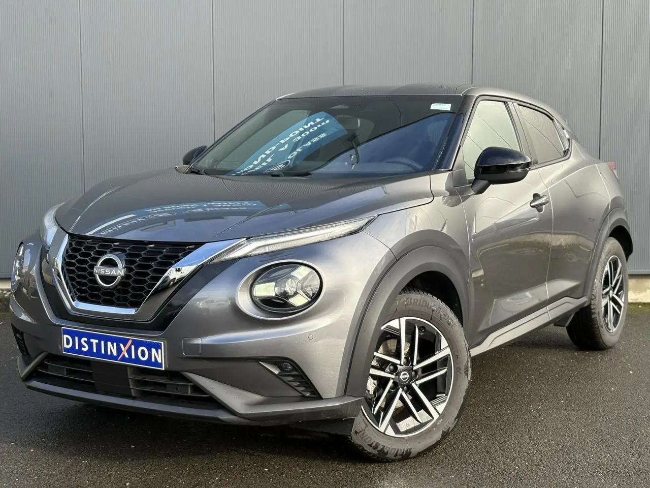 Nissan Juke 2025 gris foncé en 3/4 avant droit, avec jantes alliage diamantées et calandre chromée.