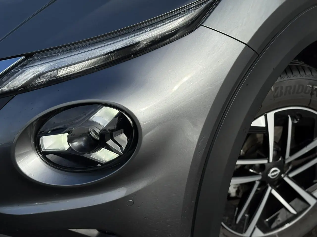 Gros plan sur le phare avant droit et la jante alliage diamantée du Nissan Juke 2025 gris foncé.