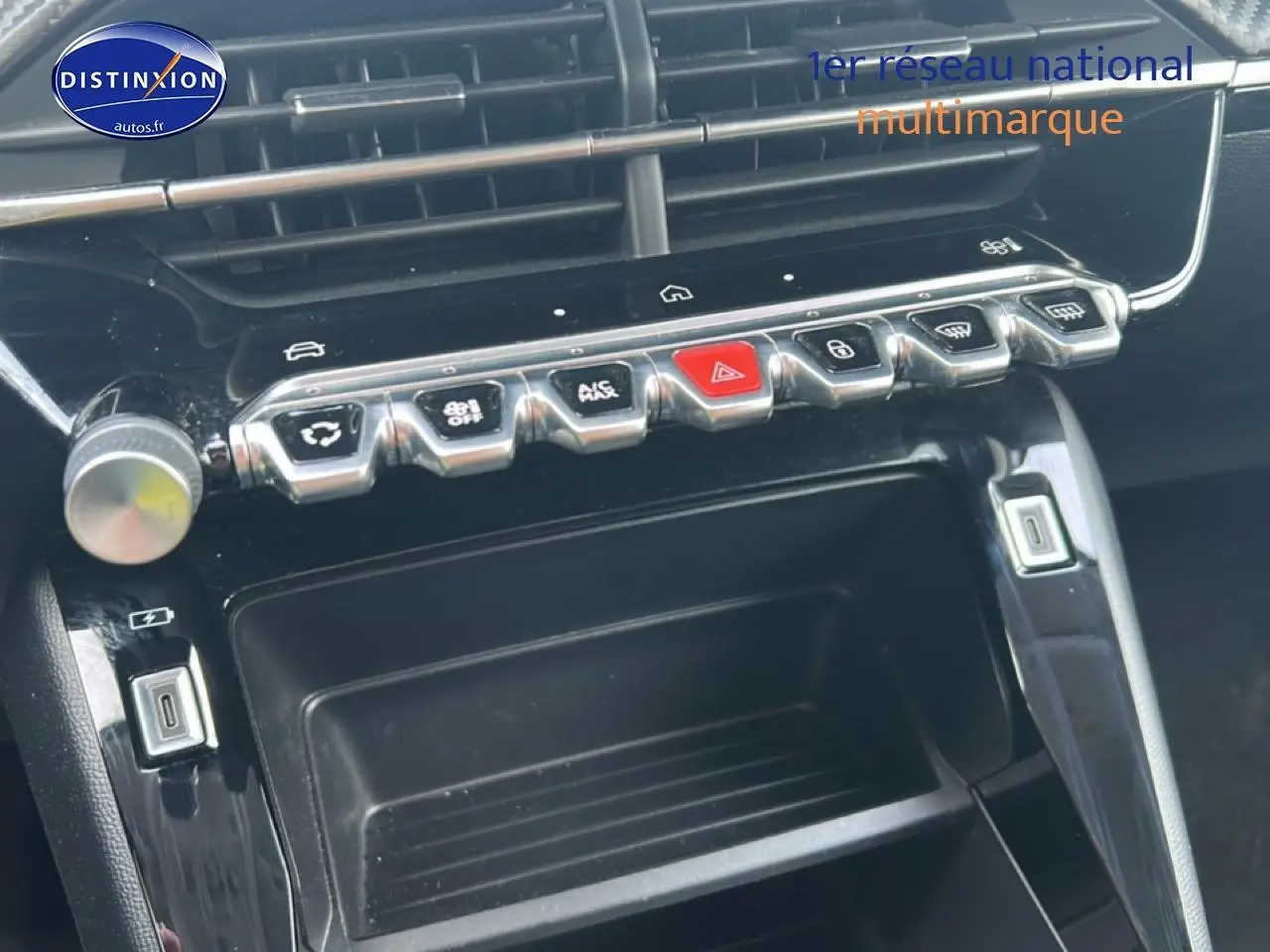 Gros plan sur la console centrale noire de la Peugeot 208 1.2 100 style, avec rangements et boutons argentés visibles.