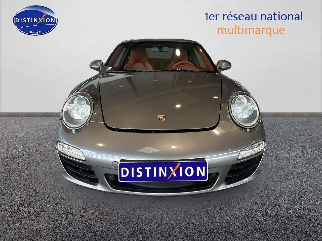 Vue frontale d'une Porsche 911 (997) Carrera PDK gris métallisé avec phares ronds et intérieur cuir marron visible.