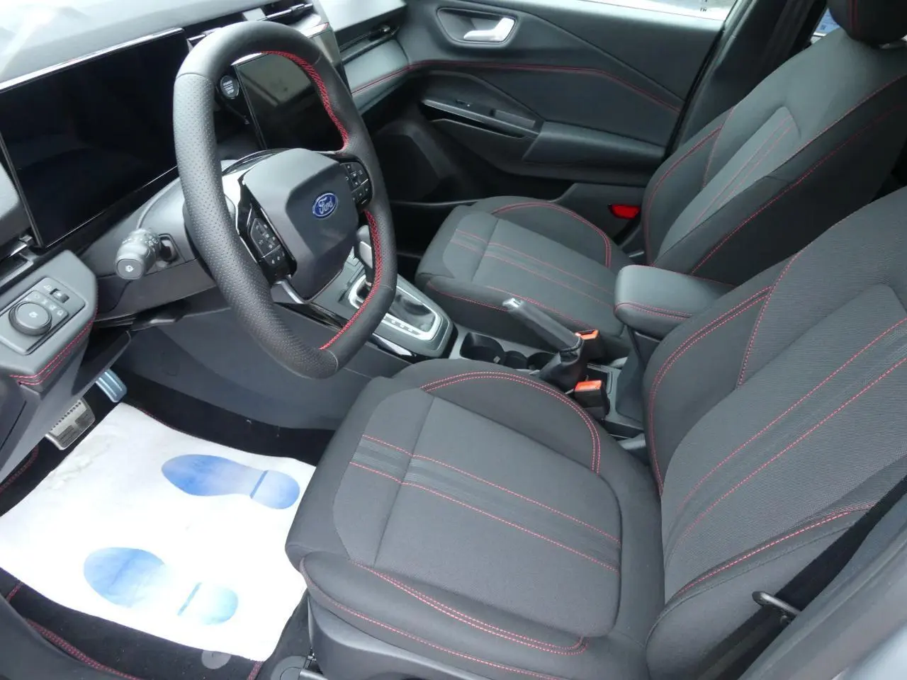 Intérieur avant du Ford Puma 2025 avec sièges tissu noirs à surpiqûres rouges et volant sport multifonction.