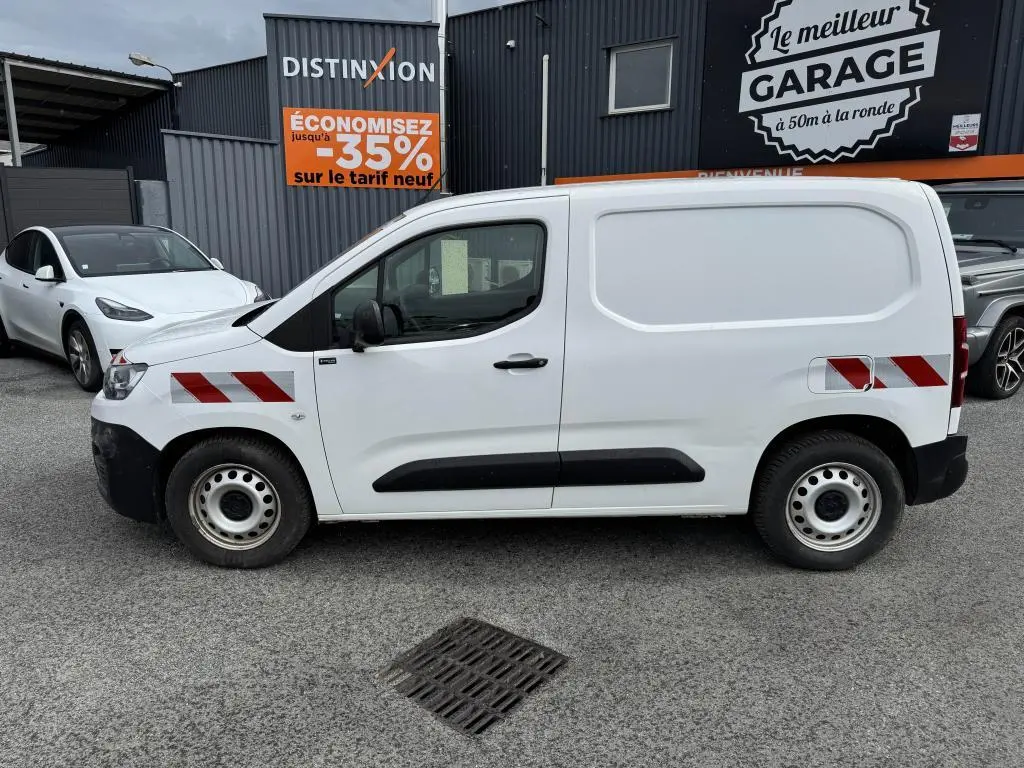 Profil côté gauche d'un utilitaire Citroën Berlingo blanc avec bandes réfléchissantes rouges et protections noires.