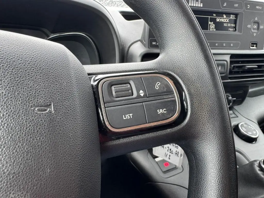 Gros plan sur les commandes au volant noir du Citroën Berlingo 2019, avec tableau de bord et écran radio en arrière-plan.