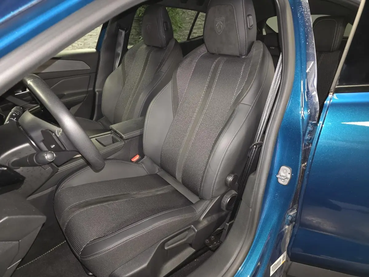 Vue intérieure côté conducteur de la Peugeot 408 bleu, sièges sport en tissu et cuir avec logo Peugeot brodé.