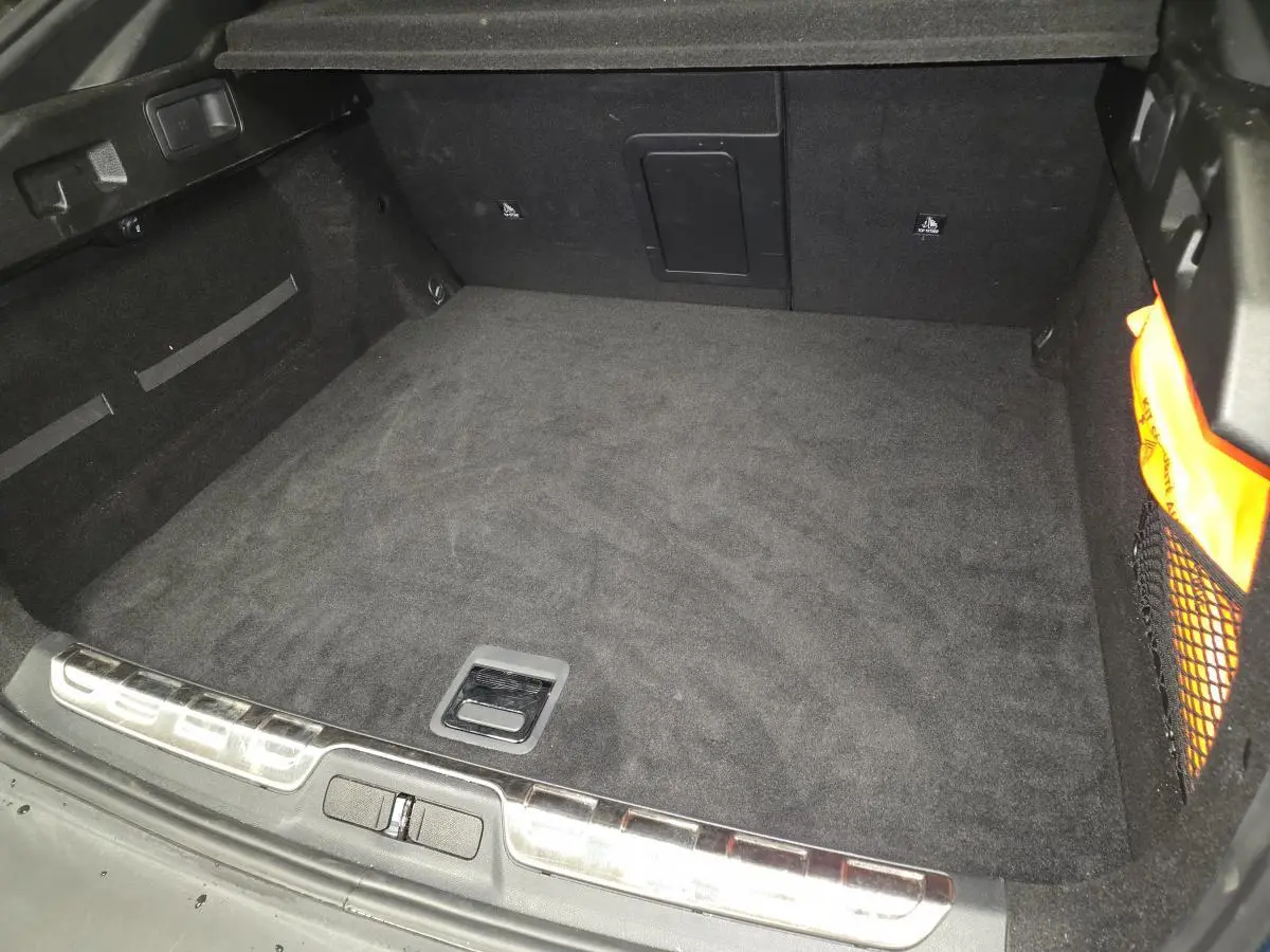 Vue plongeante sur le coffre spacieux et noir du Peugeot 408 1.6 PHEV 2024, avec filet de rangement latéral orange.