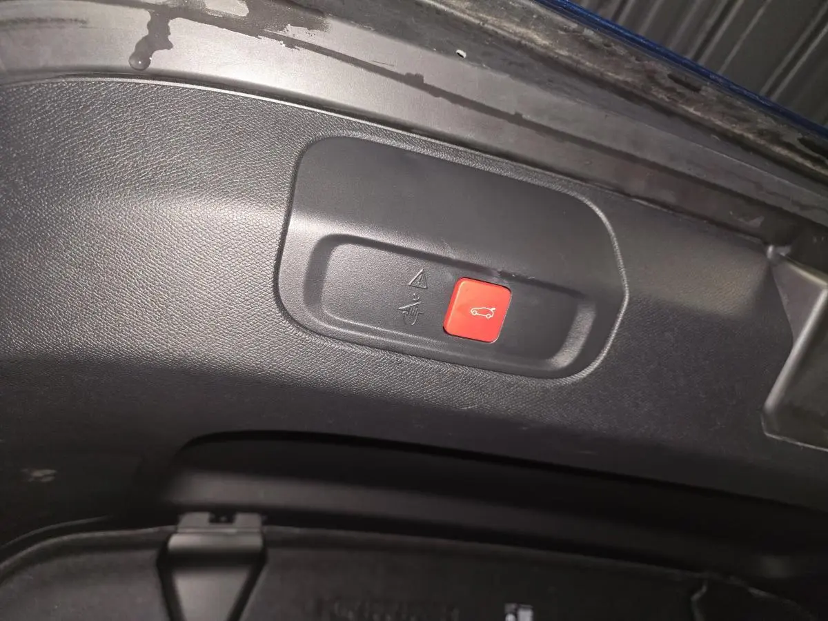 Bouton rouge d'ouverture électrique du hayon sur le panneau intérieur du coffre d'une Peugeot 408 bleu.