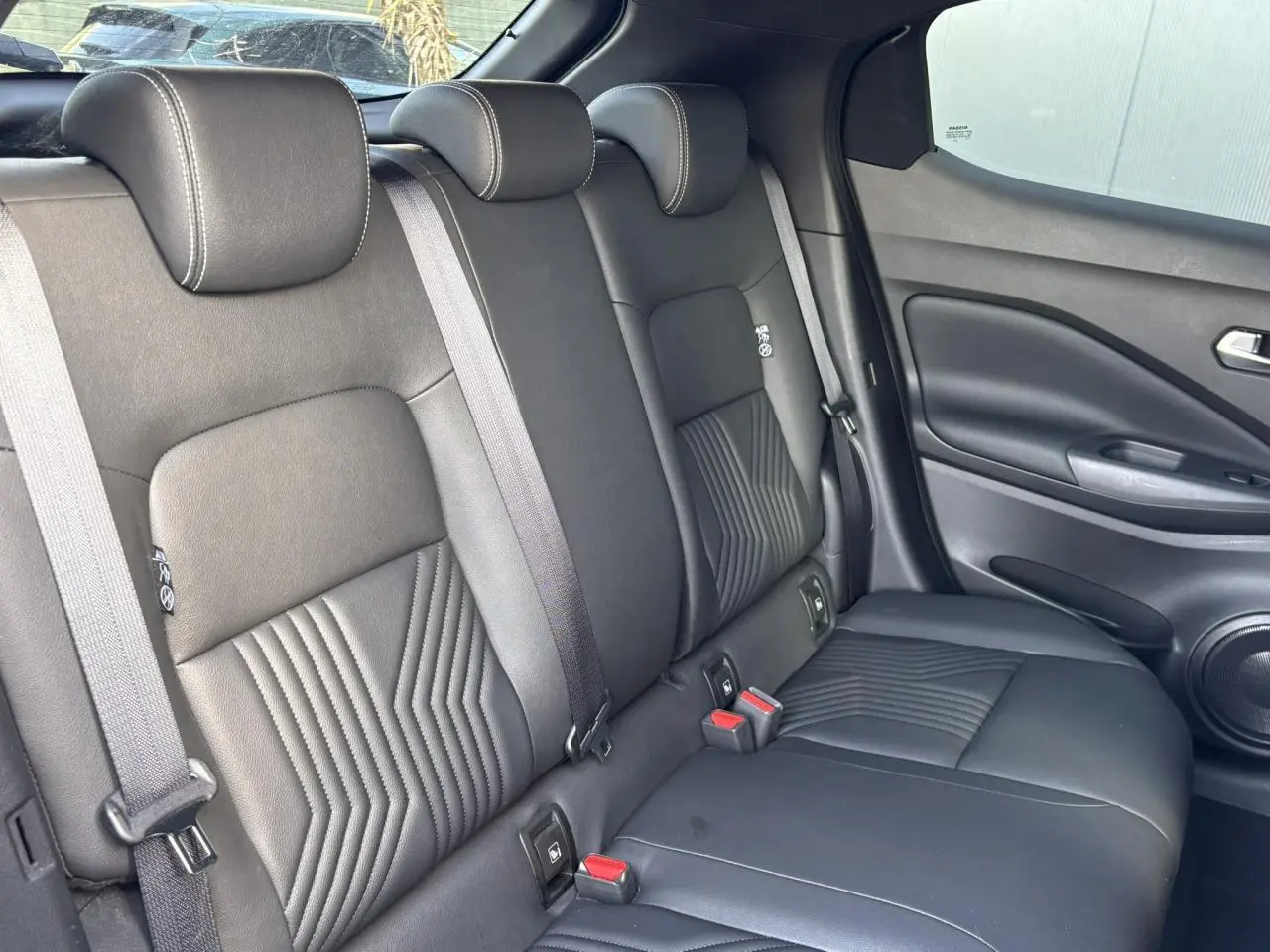 Vue intérieure arrière du Nissan Juke 2024, sièges noirs en cuir avec surpiqûres et ceintures grises visibles.