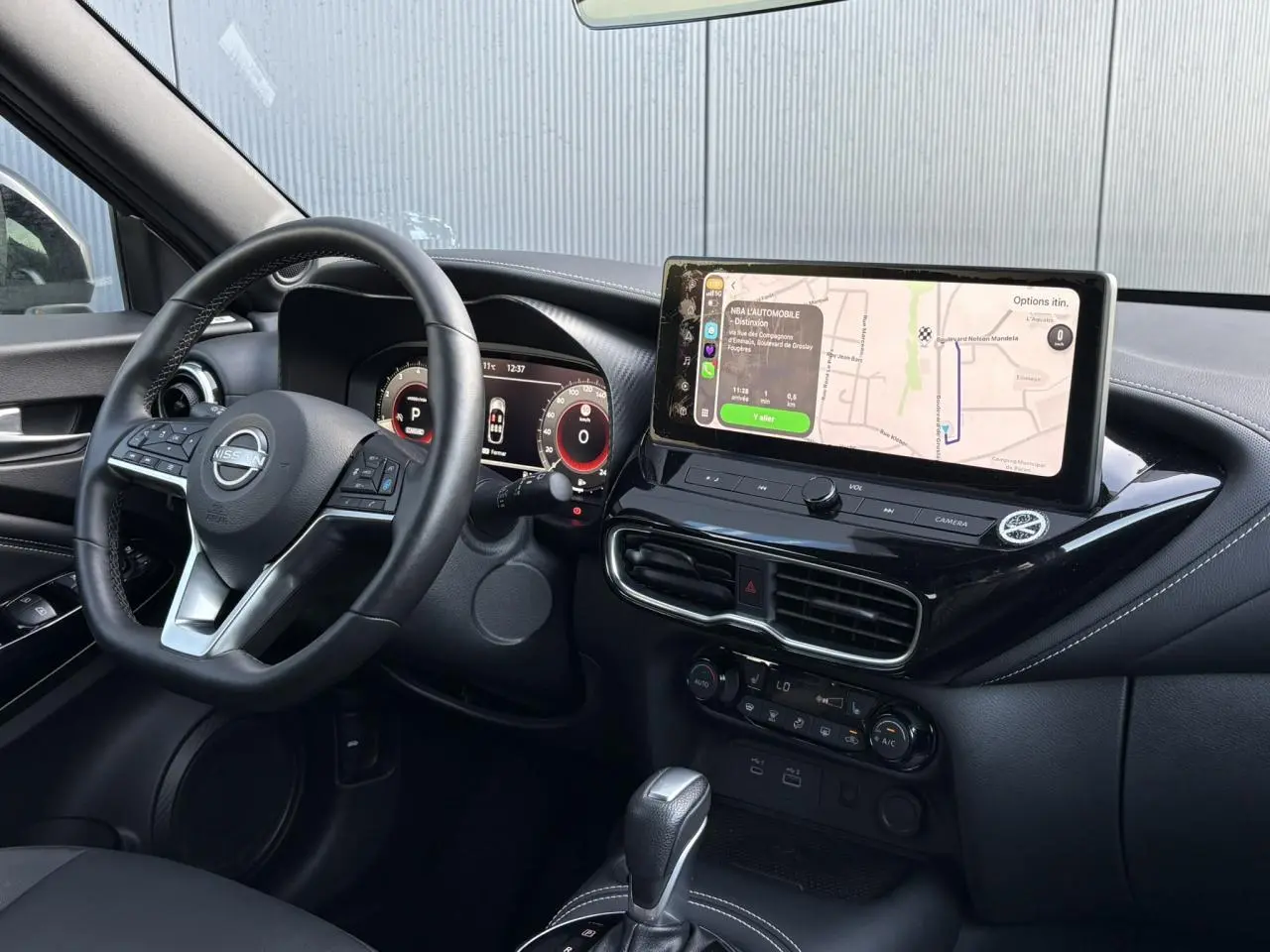 Vue intérieure côté conducteur du Nissan Juke 2024 avec tableau de bord noir et écran tactile affichant la navigation.