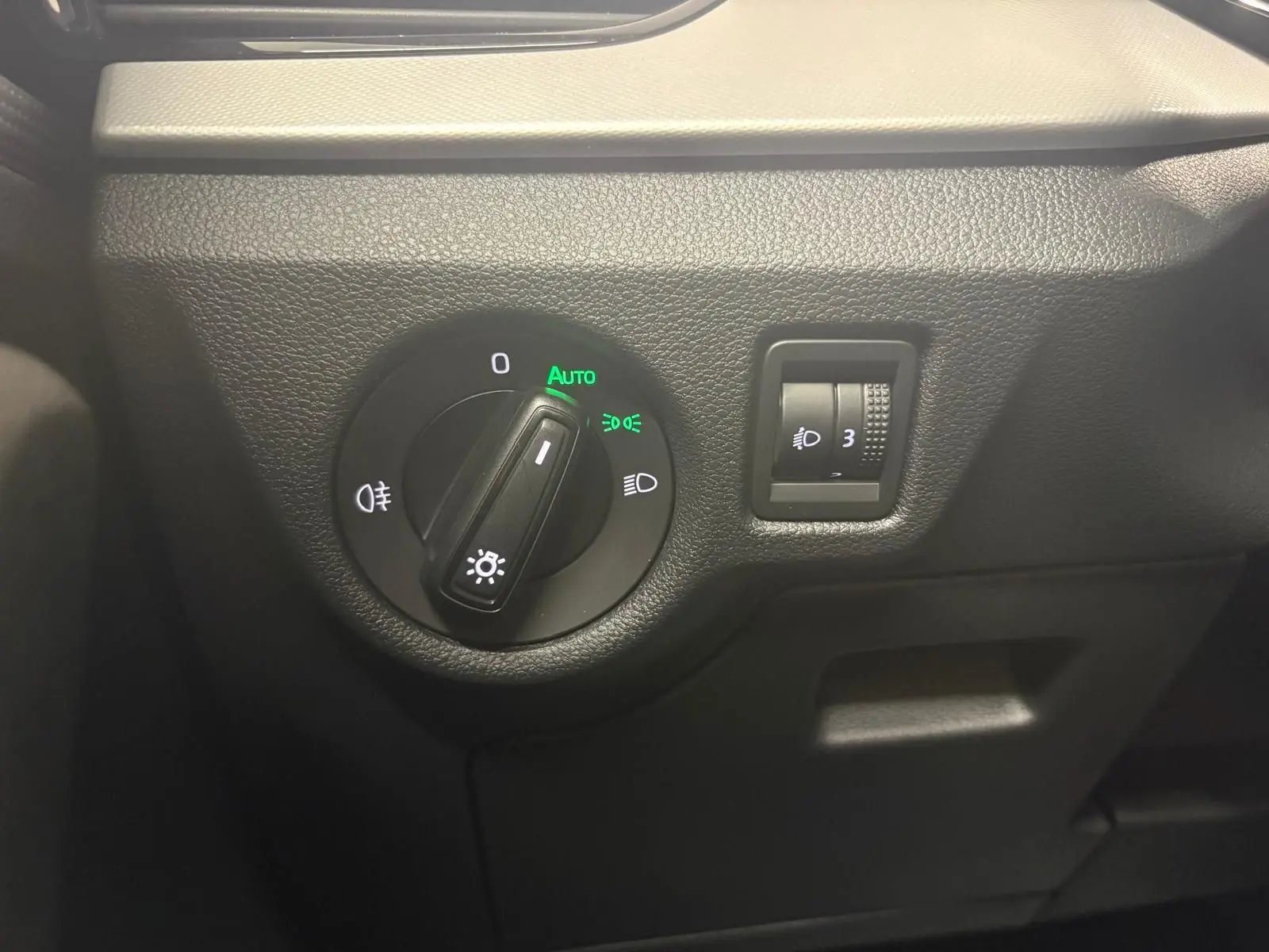 Gros plan sur la commande des phares avec réglage automatique dans l’habitacle du Skoda Kamiq gris graphite 2023.