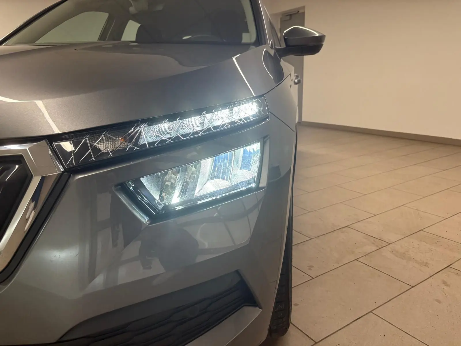 Gros plan sur l'avant droit du Skoda Kamiq 2023 gris graphite, mettant en valeur ses phares LED allumés et la calandre.