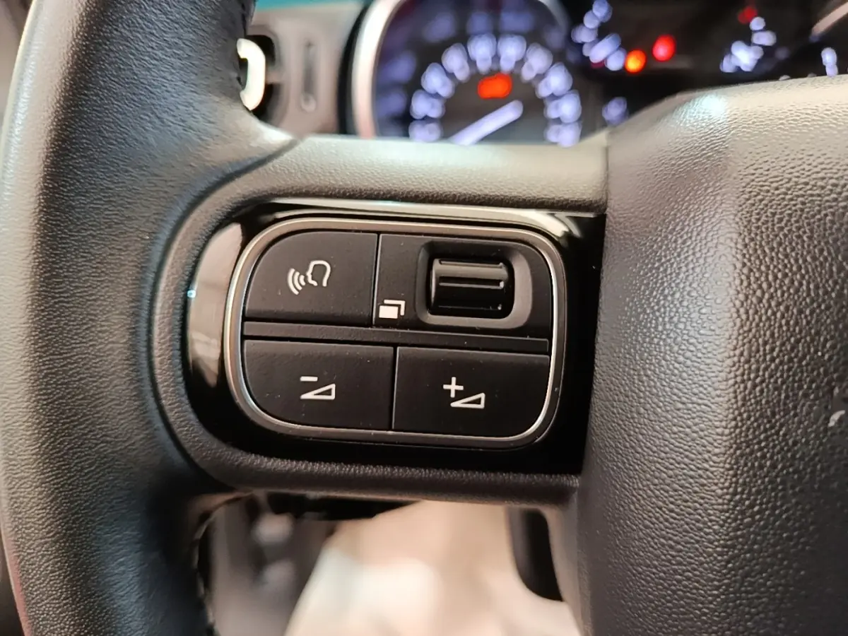 Gros plan sur les commandes du volant cuir noir de la Citroën C3 2022, avec tableau de bord flou en arrière-plan.