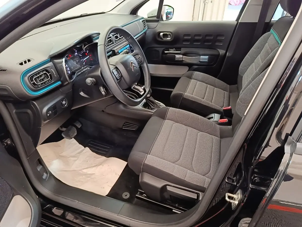 Vue intérieure côté conducteur de la Citroën C3 noire 2022, avec tableau de bord et sièges gris détaillés.