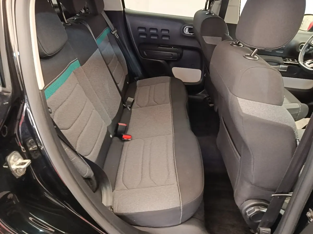 Vue intérieure côté arrière gauche de la Citroën C3 noire 2022, montrant la banquette arrière en tissu gris avec bande verte.