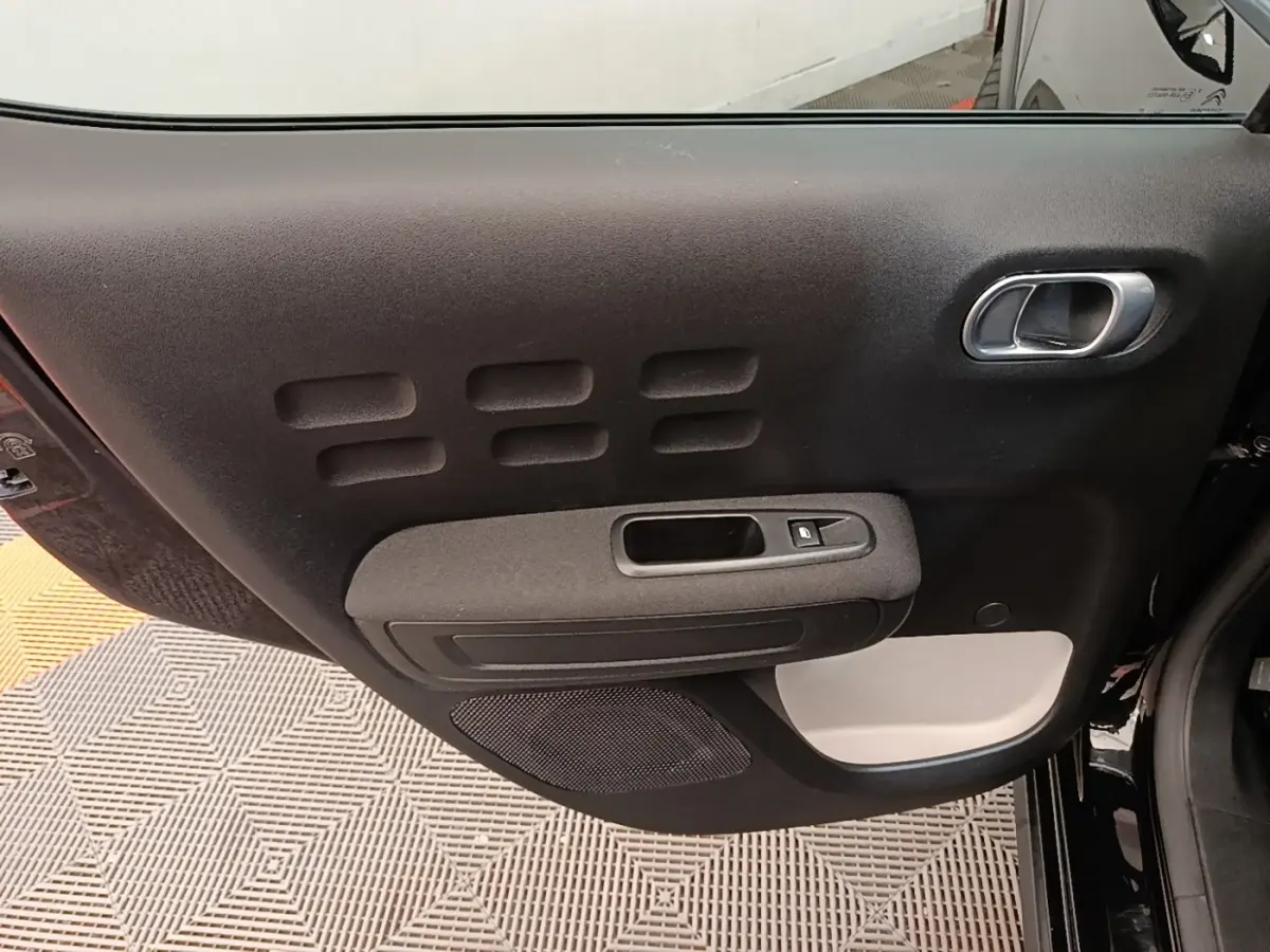 Vue rapprochée de la porte intérieure côté gauche noire de la Citroën C3 avec poignée argentée et bouton de vitre électrique.