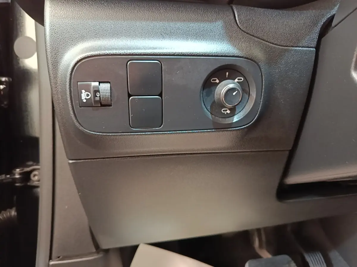Gros plan sur les commandes de réglage des phares et des rétroviseurs côté gauche intérieur d'une Citroën C3 noire 2022.