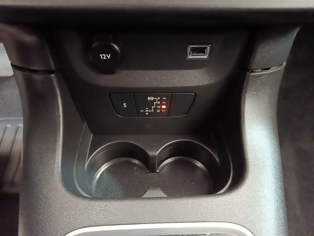 Gros plan sur la console centrale noire de la Citroën C3, avec porte-gobelets, prise 12V et indicateur de boîte auto éclairé.