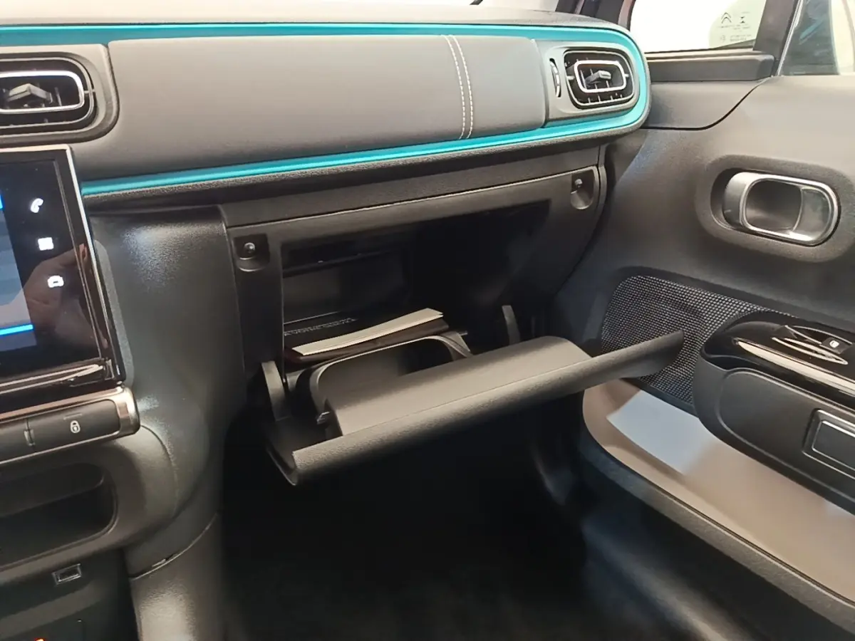 Intérieur de la Citroën C3 2022, vue côté passager sur la boîte à gants ouverte et tableau de bord noir avec liseré bleu.