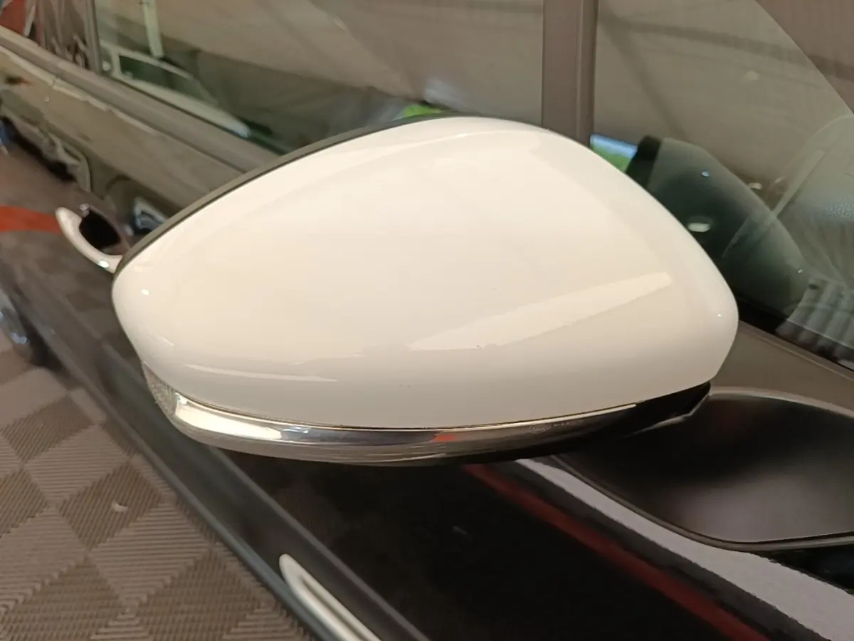 Rétroviseur blanc en gros plan côté gauche sur une Citroën C3 noire avec clignotant intégré.