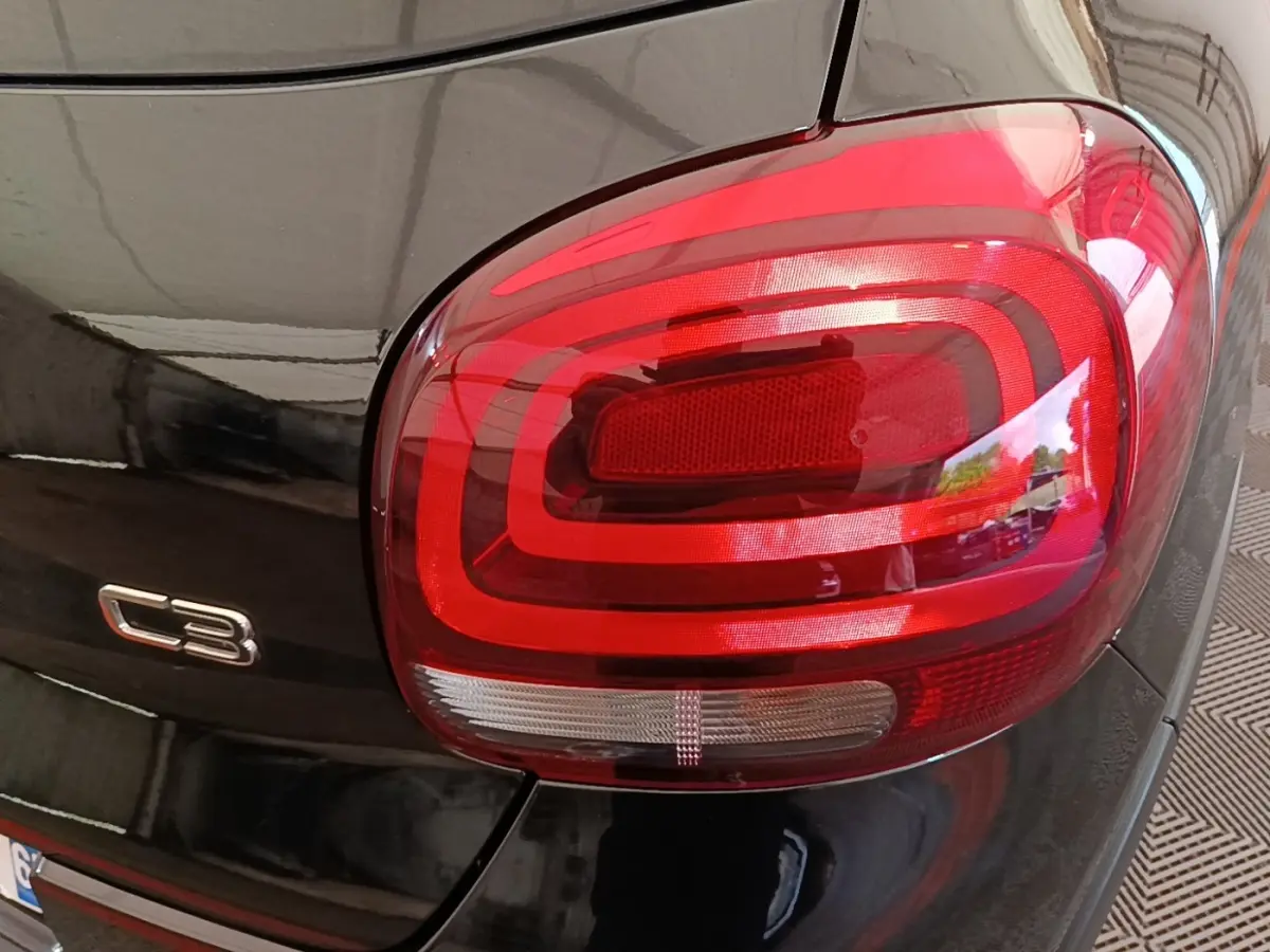 Gros plan sur le feu arrière droit rouge et le logo C3 d'une Citroën C3 noire vue de l'arrière.