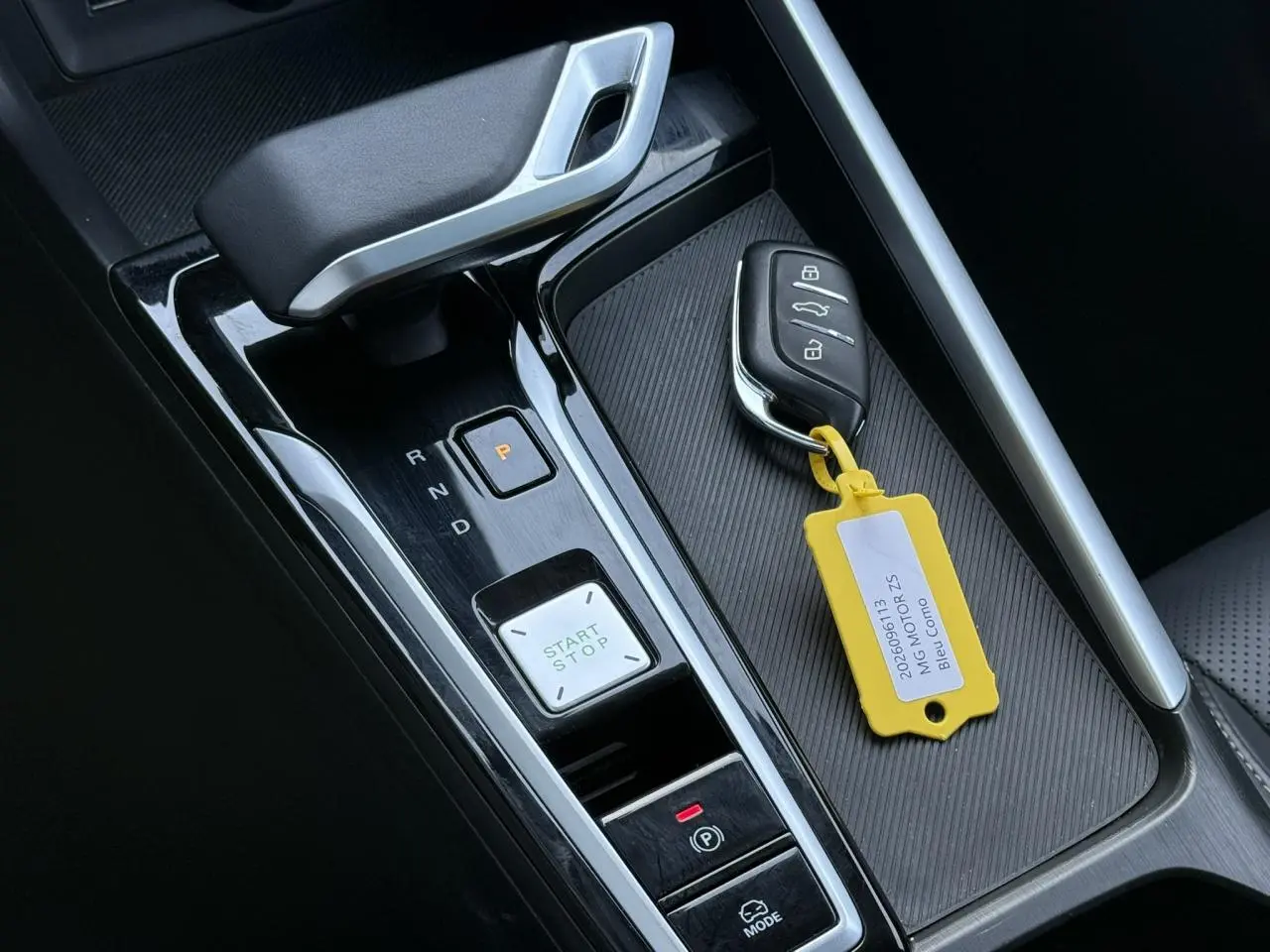 Gros plan sur la console centrale noire du MG ZS Hybrid+ 2025 avec levier de vitesse automatique et clé avec étiquette jaune.