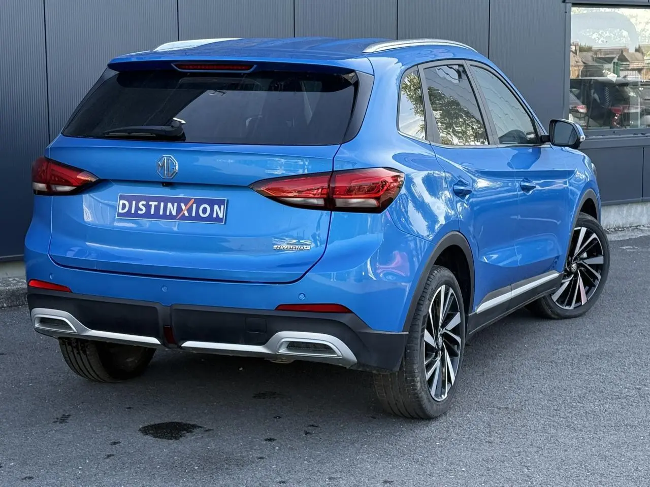 Vue 3/4 arrière droite du MG ZS 1.5 Hybrid+ 197 Luxury bleu Como avec jantes alliage 18 pouces et vitres surteintées.