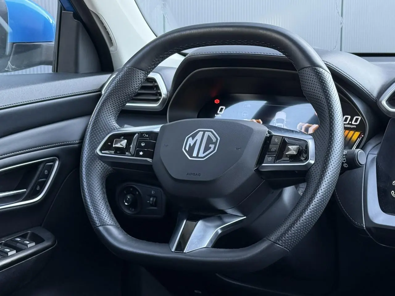 Vue rapprochée du volant en cuir perforé noir du MG ZS 1.5 Hybrid+ 197 Luxury avec tableau de bord numérique allumé.