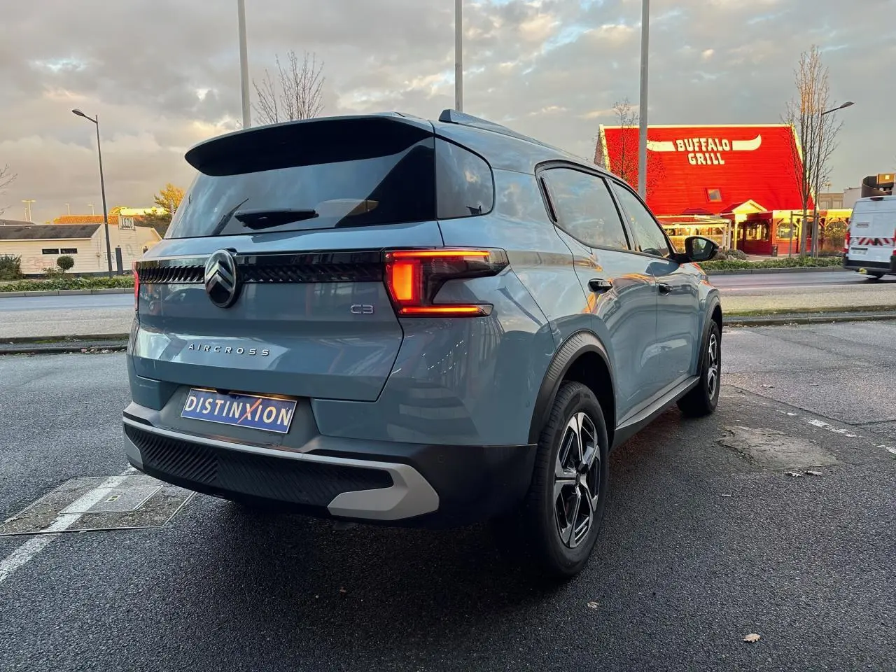 Vue 3/4 arrière droite d'une Citroën C3 Aircross bleu Monte Carlo avec toit noir et feux arrière LED allumés.