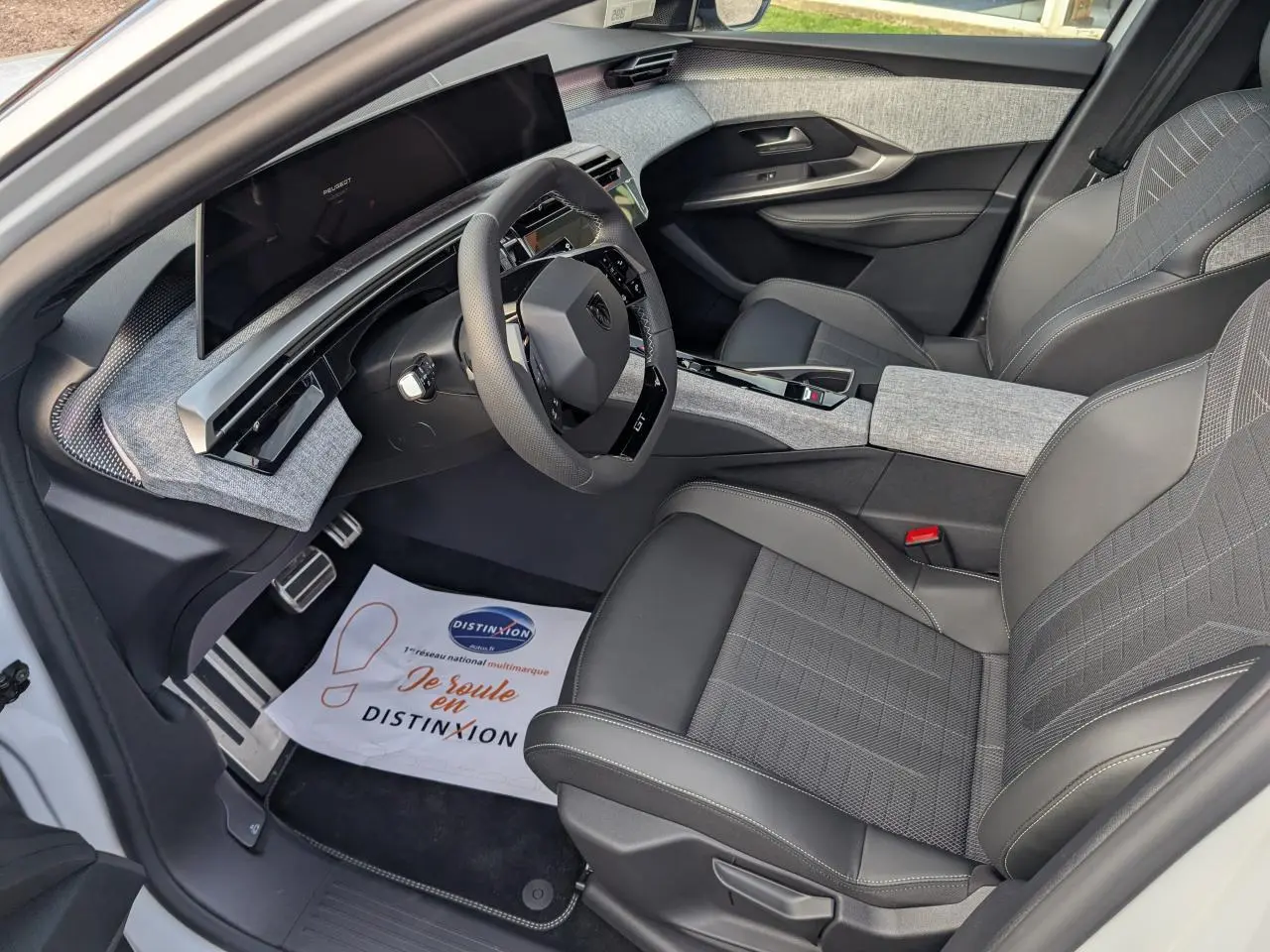 Intérieur avant droit du Peugeot 3008 blanc 2025, sellerie tissu et cuir gris, tableau de bord moderne avec écran incurvé.