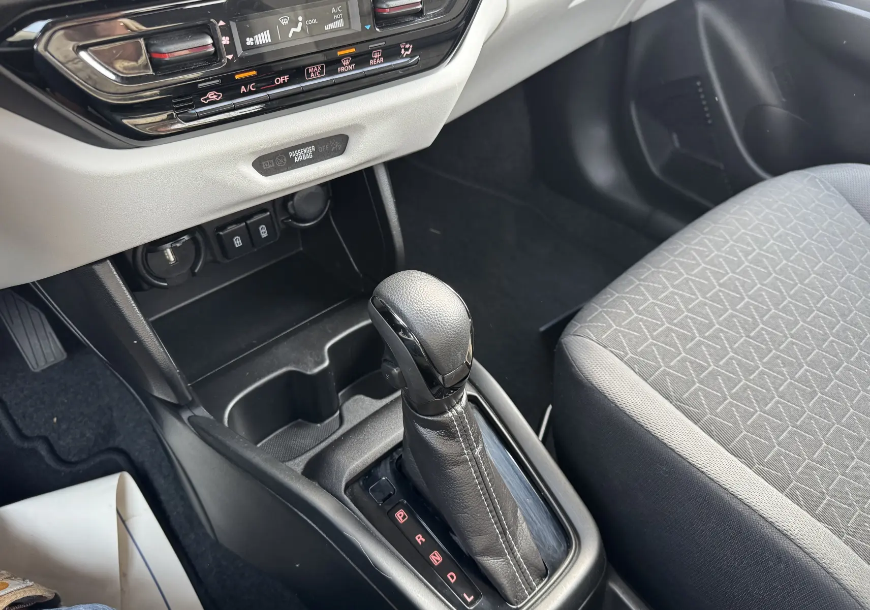 Le levier de vitesse automatique en cuir noir de la Suzuki Swift 1.2 Hybrid Privilege 2025, avec console centrale et siège tissu gris.