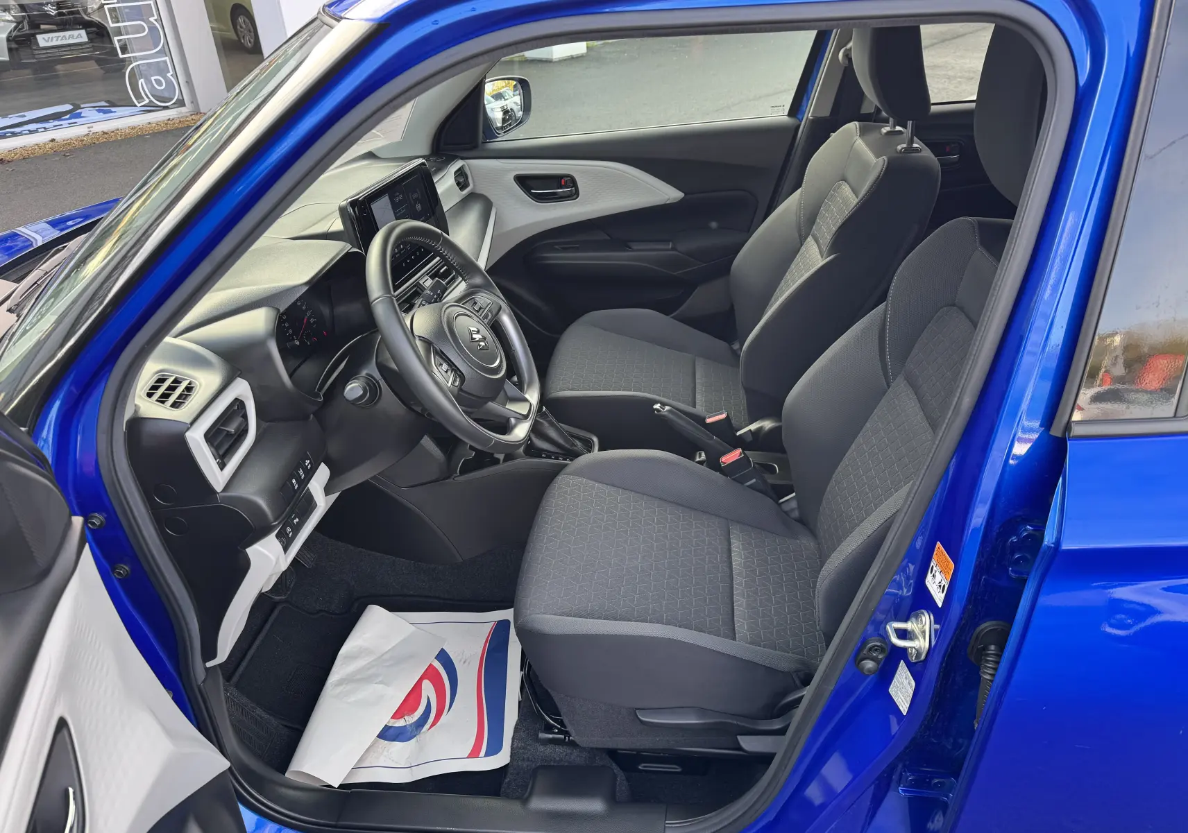 Intérieur de la Suzuki Swift 1.2 Hybrid Privilege 2025 en bleu, vue côté conducteur montrant sièges et tableau de bord moderne.