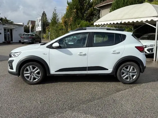 Profil côté gauche d'une Dacia Sandero Stepway blanche 2021 avec barres de toit et protections noires sur les bas de caisse.