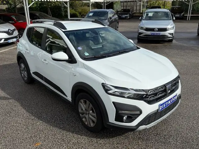 Vue 3/4 avant droite d'une Dacia Sandero Stepway blanche 2021 avec barres de toit et détails noirs contrastants.