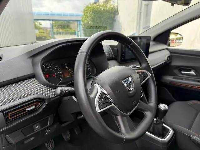 Vue intérieure centrée sur le volant Dacia et tableau de bord noir avec écran tactile et levier de vitesses manuel