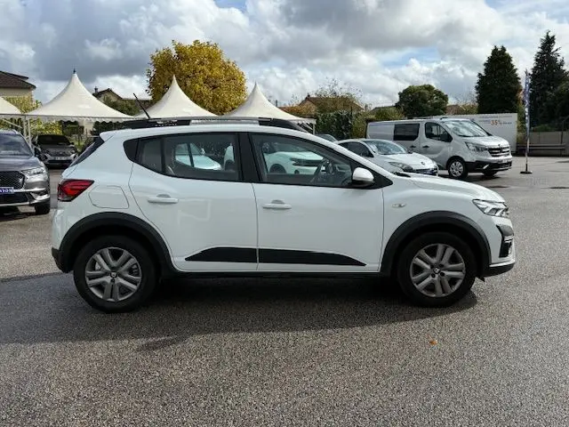 Profil droit d'une Dacia Sandero Stepway blanche 2021 avec barres de toit noires et protections latérales noires.