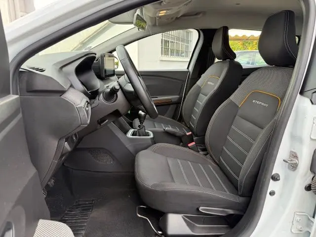 Vue intérieure côté conducteur d'une Dacia Sandero Stepway blanche 2021, sièges noirs avec surpiqûres orange et logo Stepway.