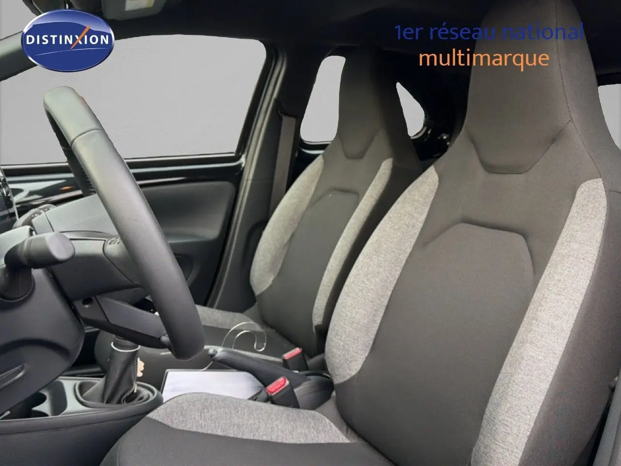 Vue intérieure côté conducteur montrant les sièges avant bi-ton gris et noir de la Toyota Aygo X 2025.