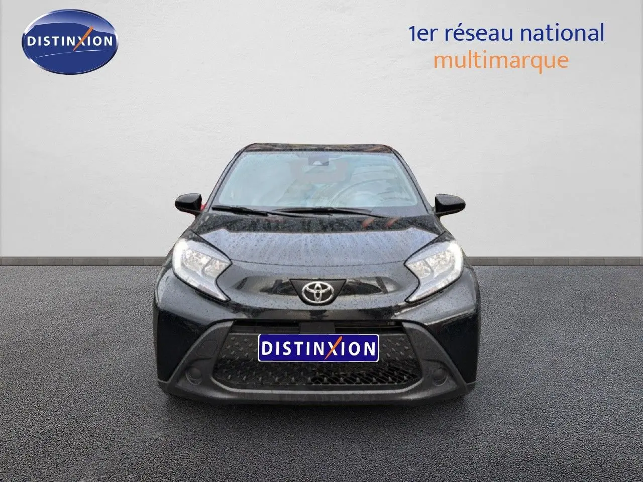 Vue de face d'une Toyota Aygo X noire 2025 avec calandre large et phares anguleux, sur fond neutre avec logo Distinxion.