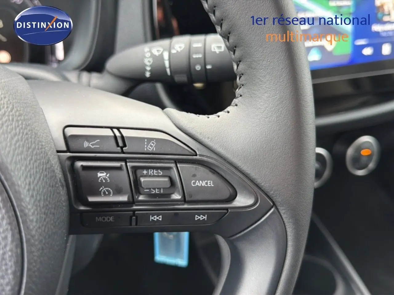 Gros plan sur les commandes au volant en cuir noir de la Toyota Aygo X 2025, avec tableau de bord flou en arrière-plan.